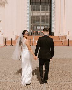 a bride and groom walking in front of a building