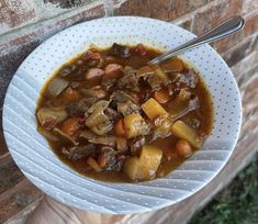 a person holding a bowl of stew in front of a brick wall