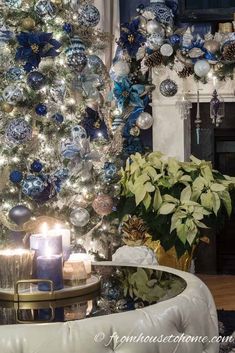 a christmas tree decorated with blue and silver ornaments, lit by a candle in front of a fireplace