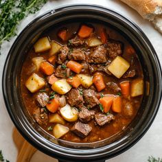 a stew in a crock pot with carrots, potatoes and meat on the side