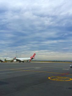 an airplane is parked on the tarmac with other planes in the background and clouds overhead