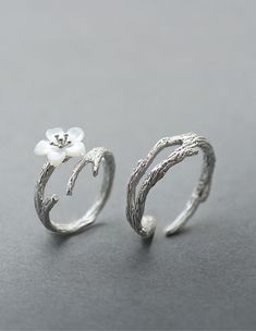 two silver rings with flowers on them sitting on top of a gray surface and one has a white flower in the middle