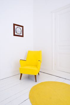 a yellow chair sitting in the corner of a room next to a white wall and rug