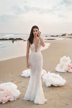 a woman standing on top of a sandy beach next to the ocean wearing a white dress