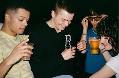 three men and one woman are looking at their cell phones while drinking beer in a bar