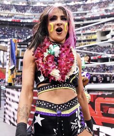 a woman with pink hair and flowers on her chest wearing black shorts in front of a stadium