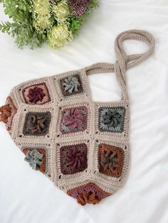 a crocheted bag sitting on top of a bed next to a bouquet of flowers