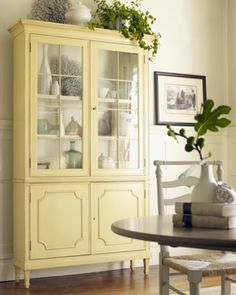 a white china cabinet sitting on top of a wooden table next to a vase filled with flowers