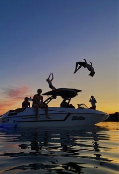 two people jumping off the back of a boat into the water at sunset with their arms in the air