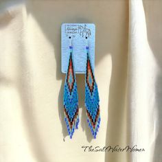 a pair of blue and red beaded earrings hanging from a hook on a white cloth