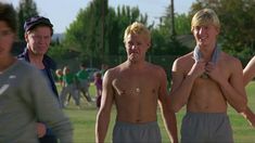 three shirtless men standing next to each other on a field with trees in the background