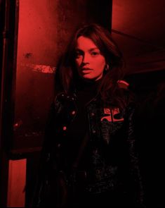 a woman standing in a dark room with red light coming from behind her and looking at the camera