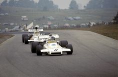 two racing cars driving down the road with people watching from the sidelines behind them