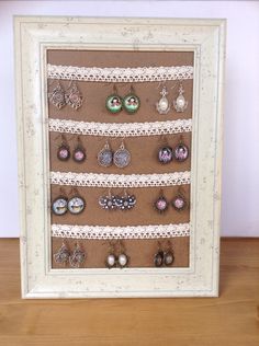 a white frame holds several pairs of earrings on display in front of a wooden table