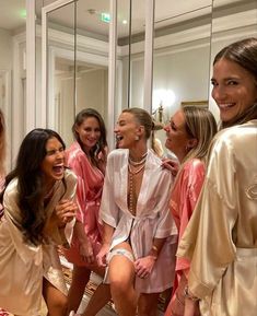 a group of women standing next to each other in front of a mirror wearing robes