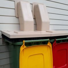 three plastic containers are hanging on the side of a house, with one yellow and one red