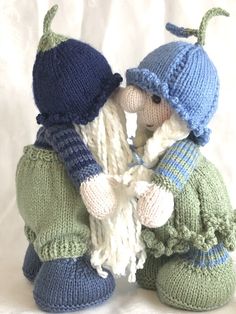 two knitted dolls are sitting next to each other on a white background, one is wearing a blue and green hat