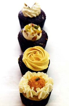 four cupcakes with different toppings are lined up on a white table top