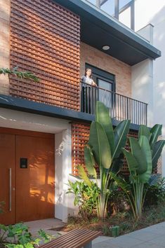 a person standing on a balcony next to a wooden door and some plants in front of it