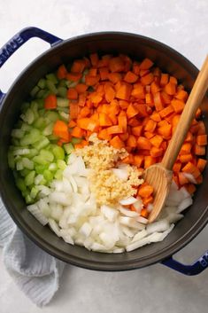 carrots, celery and onions are being cooked in a pot with a wooden spoon