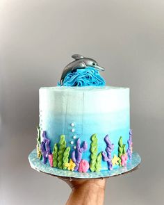 a hand holding a cake decorated with blue frosting and sea animals on the top