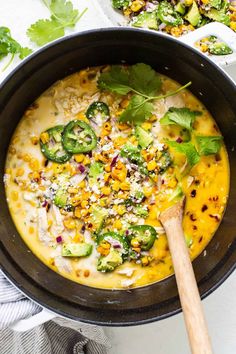 a skillet filled with cheese and vegetables on top of a white table next to a wooden spoon