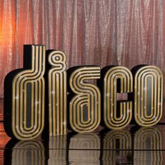 the word disco spelled out in gold letters on a black and silver surface with a red curtain behind it