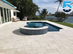 an empty swimming pool in front of a house with palm trees and water behind it