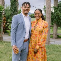 a man and woman standing next to each other in front of an outdoor area with trees