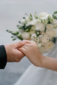 the bride and groom are holding hands over their wedding bouquet with white flowers in the background