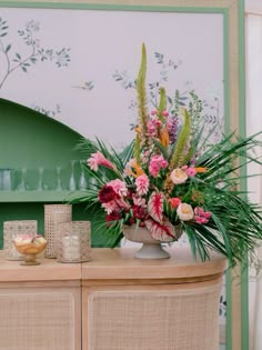 a vase filled with lots of flowers on top of a wooden table next to a green cabinet