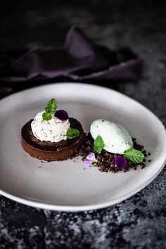 two desserts on a white plate sitting on a black tablecloth with purple flowers