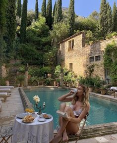 a woman sitting at a table next to a pool drinking from a bottle and eating