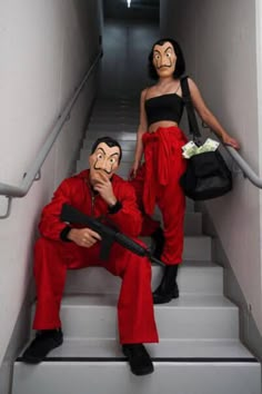 two people in red pants and black tops with fake masks on their faces are sitting down the stairs