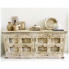 an old white wooden cabinet with decorative items on the top and bottom, sitting against a wall