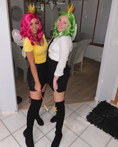 two women dressed in costumes standing next to each other on a tile floor, one with pink hair and the other green