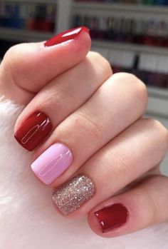 a woman's hand with red and pink manicures on it, while she holds