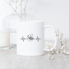 a white coffee mug sitting on top of a table next to a vase with flowers