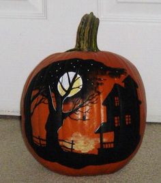 a carved pumpkin sitting on the ground in front of a door with a tree and house painted on it