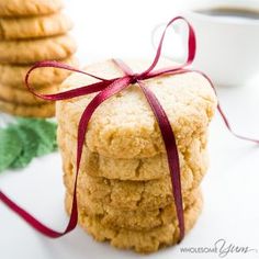 a stack of cookies with a red ribbon tied around the top and two cups of coffee in the background