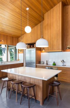 a large kitchen with wooden cabinets and white counter tops, along with three stools