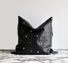 a black leather pillow with silver studs on the front and back, sitting on a marble surface