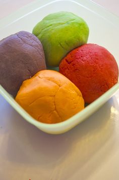 four different colored pastries in a white bowl on a table top, with one orange and one green