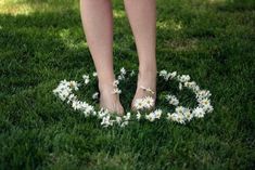 a woman standing in the grass with daisies on her feet