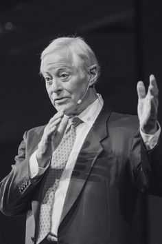 an older man wearing a suit and tie giving a speech with his hands in the air