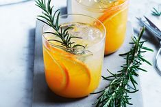 two glasses filled with orange juice and garnished with rosemary