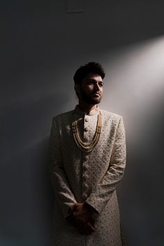 a man standing in front of a wall wearing a white suit and gold chain necklace