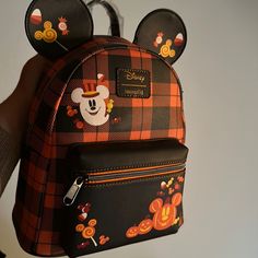 a person holding a mickey mouse backpack with ears on it's head and an orange plaid pattern