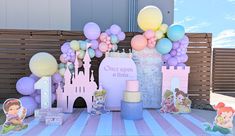 a table topped with lots of balloons and princess themed items on top of a striped table cloth