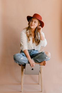 a woman sitting on top of a wooden chair wearing a red hat and white shirt